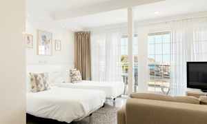 Et lyst hotelværelse med to enkeltsenge, store vinduer og havudsigt. (AI-genereret tekst)