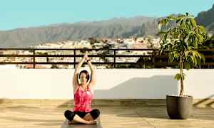 Person sidder i yogastilling på en terrasse med udsigt over byen og bjergene. (AI-genereret tekst)
