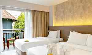 To opdækkede enkeltsenge med dekorative håndklæder og blomster. Udsigt over en møbleret altan med grønne områder og bygning. (AI-genereret tekst)