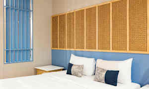 Et soveværelse med en seng, puder og en blå væg med flettede paneler. (AI-genereret tekst)