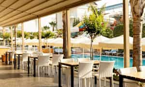 Udendørs restaurant ved en pool med parasoller og liggestole i baggrunden. (AI-genereret tekst)