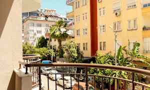 Udsigt fra en altan mod en gade omgivet af bygninger og grønne områder. (AI-genereret tekst)