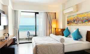 Hotelværelse med en stor seng, blå puder og havudsigt fra balkonen. (AI-genereret tekst)