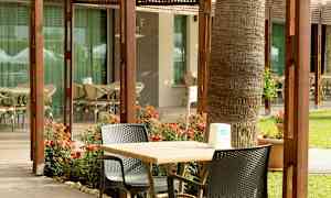 En terrasse med borde, stole og blomster foran en bygning med glasvinduer. (AI-genereret tekst)