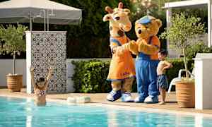 To maskotkarakterer, en giraf og en bjørn, står ved poolen udendørs. (AI-genereret tekst)