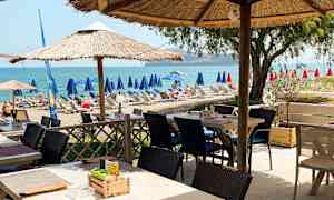 En udendørs servering med parasoller nær en strand med liggestole og udsigt over havet. (AI-genereret tekst)