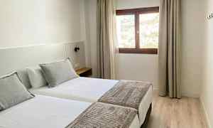 Et hotelværelse med to enkeltsenge, et vindue med lysindfald og del af udsigten udenfor. (AI-genereret tekst)