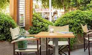 Udendørsmiljø med bord og stole ved siden af grønt. (AI-genereret tekst)