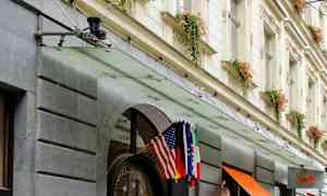 Hotelfacade med indgang dekoreret med blomsterkrukker og flag. (AI-genereret tekst)