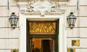 Indgang til bygning med skilt Antica Roma, omgivet af to flag og planteudsmykning. (AI-genereret tekst)