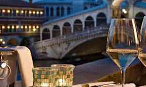 En tallerken med skaldyr og et glas hvidvin på et bord med udsigt over en oplyst bro i skumringen. (AI-genereret tekst)