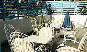 En terrasse med hvide havemøbler og borde, omgivet af et blåmalet hegn og blomstrende buske. (AI-genereret tekst)