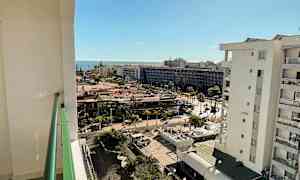 Udsigt fra en altan over et byområde med havet i baggrunden og solskin. (AI-genereret tekst)