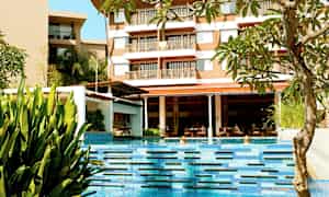 En pool med klart blåt vand omgivet af planter og et hotel i baggrunden. (AI-genereret tekst)