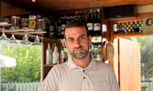 En hvid skjorte ved en bar med hylder fyldt med flasker i baggrunden, samt et cocktailglas med en farvet drik foran sig. (AI-genereret tekst)