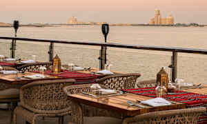 En udendørs restaurant med opdækkede borde og udsigt over havet ved solnedgang. (AI-genereret tekst)