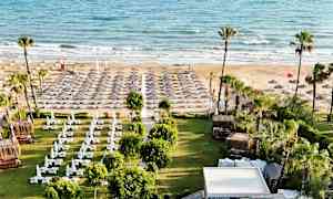 Billede af en strand med liggestole og parasoller samt et grønt område med skyggegivende tag foran. (AI-genereret tekst)