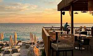 En solnedgang ved havet med en restaurantterrasse og solsenge på stranden. (AI-genereret tekst)