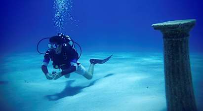 En dykker under vandet tæt på en antik søjle på havbunden. (AI-genereret tekst)