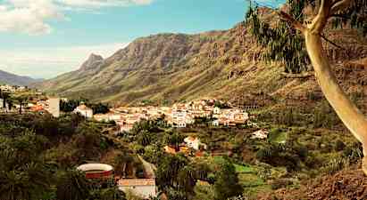 En bjerglandsby med hvide huse og røde tage beliggende i en grøn dal omgivet af høje bjerge. (AI-genereret tekst)
