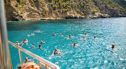 Badesende personer i klart blåt vand foran en klippekyst. (AI-genereret tekst)