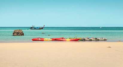 Flere kajakker på en sandstrand, med havet og en båd i baggrunden. (AI-genereret tekst)