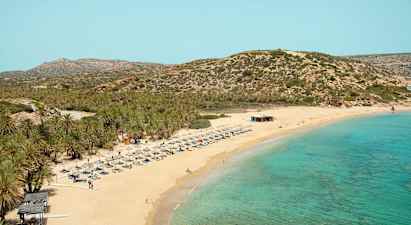 Sandstrand med turkis hav, liggestole og parasoller. Baggrund med bevoksede bjerge. (AI-genereret tekst)