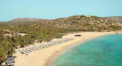 Sandstrand med turkis hav, liggestole og parasoller. Baggrund med bevoksede bjerge. (AI-genereret tekst)