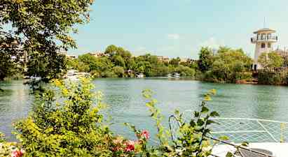 En flod med grønne buske og træer langs dens kanter. En fyrtårn-lignende bygning ses til højre. (AI-genereret tekst)