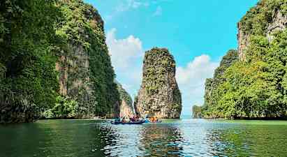 Flere personer padler kajakker gennem en naturskøn passage mellem høje, grønne klipper. (AI-genereret tekst)