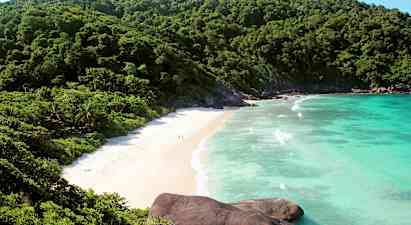 Billede af en strand omgivet af grønne bjerge og blåt hav. (AI-genereret tekst)