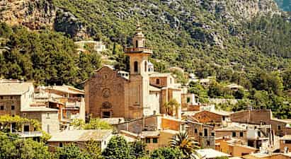 Stenkirke med tårn omgivet af en landsby blandt bjerge og grønne områder. (AI-genereret tekst)