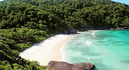 Billede af en strand omgivet af grønne bjerge og blåt hav. (AI-genereret tekst)