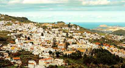 Udsigt over en by med mange hvide bygninger beliggende i en frodig dal nær havet. (AI-genereret tekst)