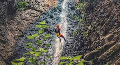 Person, der rapellerer ned ad et vandfald med reb, omgivet af klipper og vegetation. (AI-genereret tekst)
