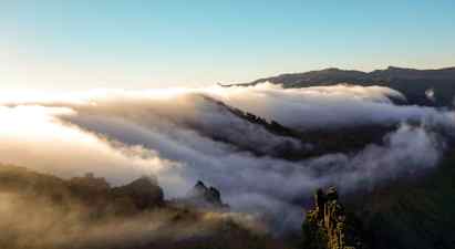 Skyer driver hen over en bjergkæde ved solopgang eller solnedgang. (AI-genereret tekst)