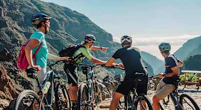 En gruppe mennesker med mountainbikes kigger på en naturskøn udsigt mellem bjerge med grønnende dale. (AI-genereret tekst)