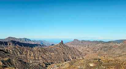 Landskab med bjerge og en markant klippeformation under blå himmel. (AI-genereret tekst)