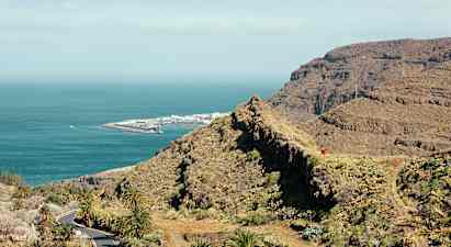 Udsigt over bjergrigt landskab og kyst med hav og en havneanlæg. (AI-genereret tekst)