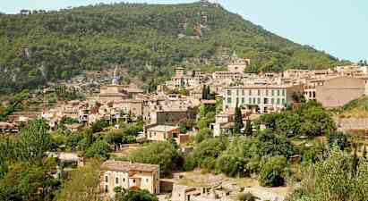 Billede af en bjerglandsby med flere stenhuse omgivet af frodig vegetation. (AI-genereret tekst)