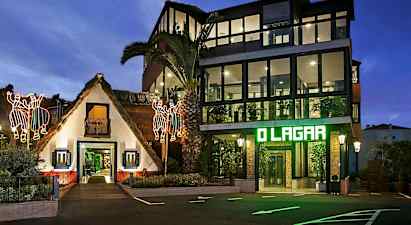 En bygning med en traditionel stråtækt struktur og en moderne glaspanelsbygning ved siden af, oplyst om aftenen med lysende dekorationer og belysning. (AI-genereret tekst)