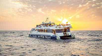 En glasbundsbåd med mennesker ombord sejler på havet under en solnedgang. (AI-genereret tekst)