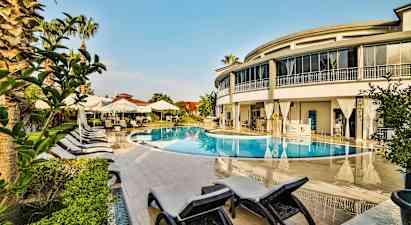 En udendørs pool omgivet af liggestole, parasoller og en moderne bygning. (AI-genereret tekst)