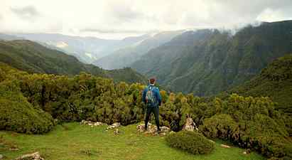 En person står på en grøn høj med udsigt over skovklædte bjerge. (AI-genereret tekst)