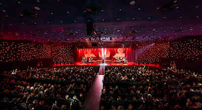 En koncertsal med en oplyst scene, hvor forskellige musikere optræder foran et publikum. (AI-genereret tekst)