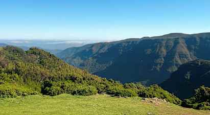 Billedet viser et landskab med frodige bakker og bjerge under en klar blå himmel. (AI-genereret tekst)