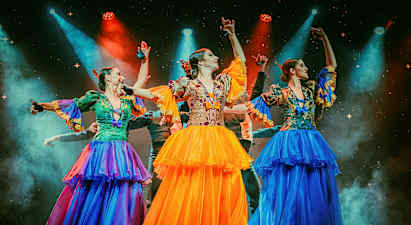 Tre personer iført farverige traditionelle dragter danser på en oplyst scene. (AI-genereret tekst)