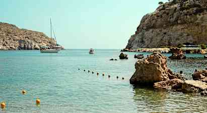 En bugt med klart vand og stenede kystlinje, hvor en båd og et mindre fartøj ses i baggrunden. (AI-genereret tekst)