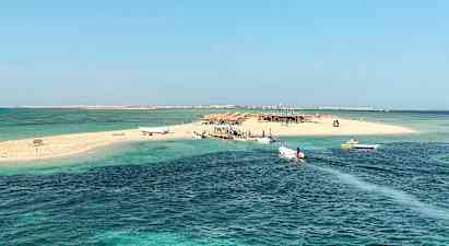 En lille sandø med både ved broen, omgivet af klart blåt vand. (AI-genereret tekst)