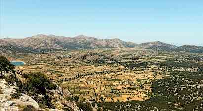 En bred dal omgivet af bjerge med græsgange og marker. (AI-genereret tekst)